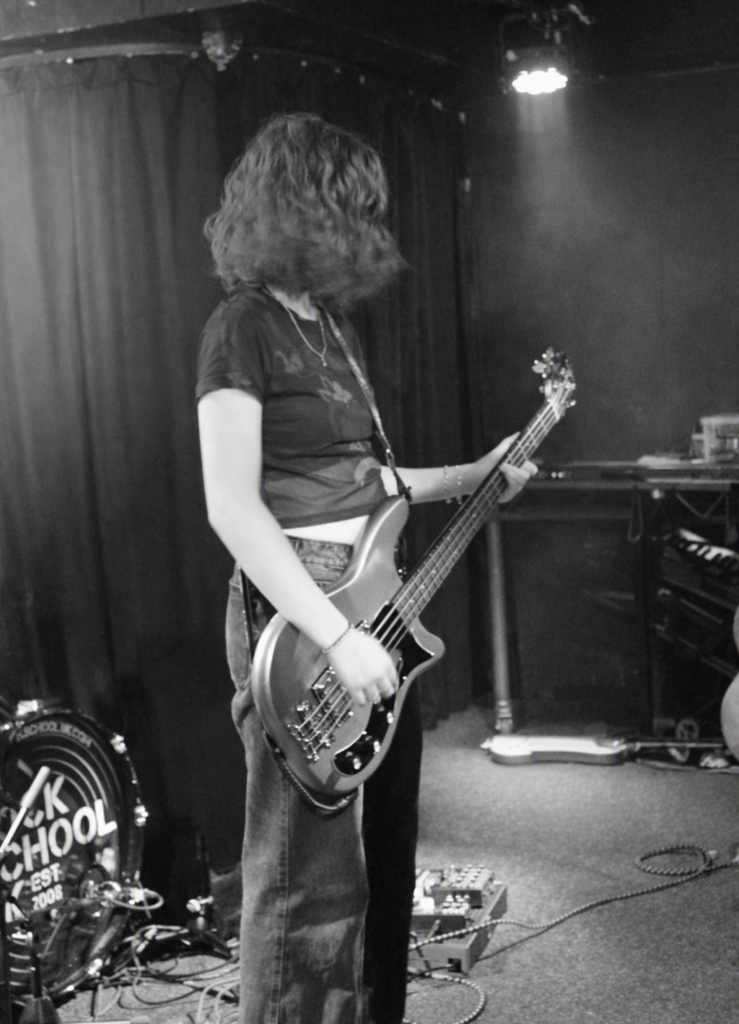 Lottie performing live on stage, playing bass during a Rock School UK session, part of her Just a Girl with a Bass artist page.